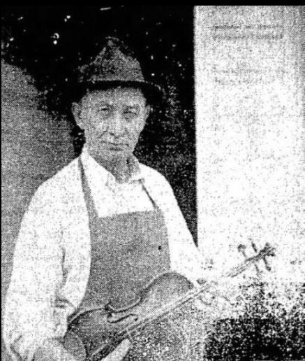 Tutterway as older man holding violin by his shop